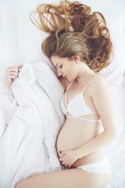 tranquil portrait of beautiful pregnant woman lying in bed, top view - Photo, Image