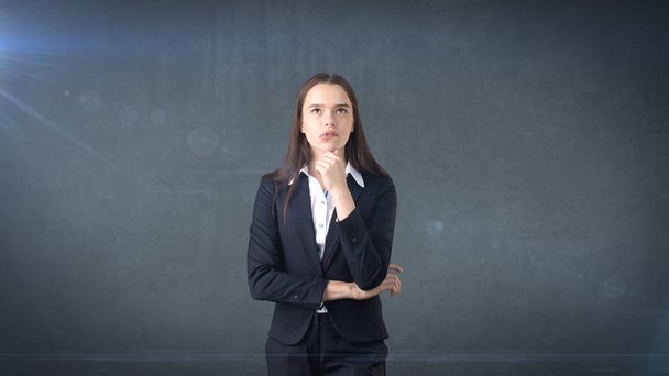 Beautiful businesswoman with arms folded looking up at copyspace. Biting her lips. - 写真・画像