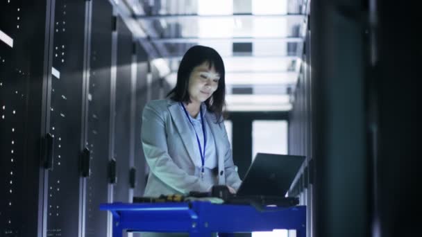 Азиатский инженер по информационным технологиям работает над портативным компьютером в большом центре обработки данных, полном стеллажных серверов
. - Кадры, видео