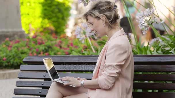 Attractive blonde white woman working freelance with laptop and smartphone in park at sunny day - Metraje, vídeo