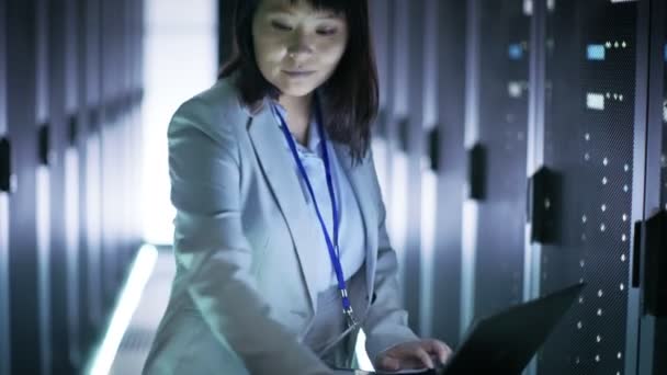 Asyalı kadın mühendis bir kilitlenme sepeti dizüstü bilgisayarda çalışan, o sabit diskleri tarar. İçinde büyük bir kız datacenter tam, raf tipi sunucular. - Video, Çekim