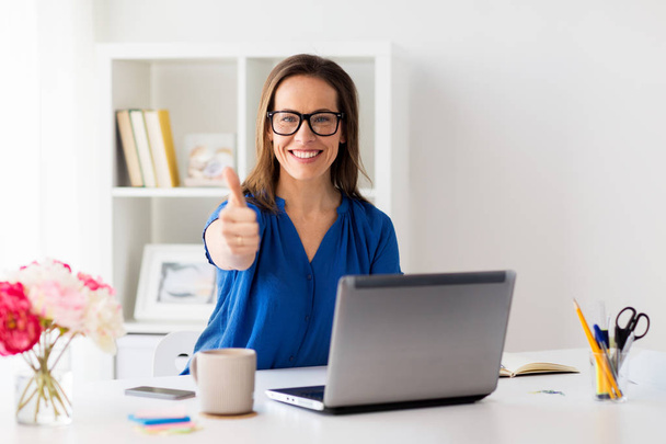 woman with laptop showing thumbs up at office - Foto, Imagen