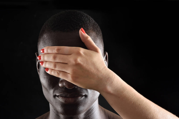 a hand covering a eyes of african man on black - Foto, imagen