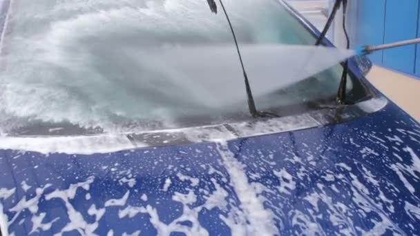 Lavado de autos. Un chorro de agua con una fuerte presión lava la espuma del vidrio del coche
 - Imágenes, Vídeo