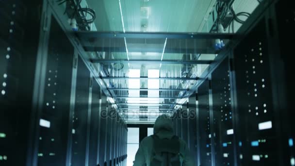 Siguiendo a Shot of a Hacker en una sudadera con capucha caminando en el centro de datos y conectándose al servidor Rack
. - Imágenes, Vídeo