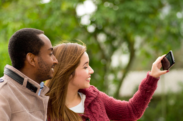 Beautiful and smiling happy interracial young couple in parl taking a selfie - Фото, зображення