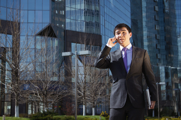 Young businessman standing and talking on mobile phone - 写真・画像