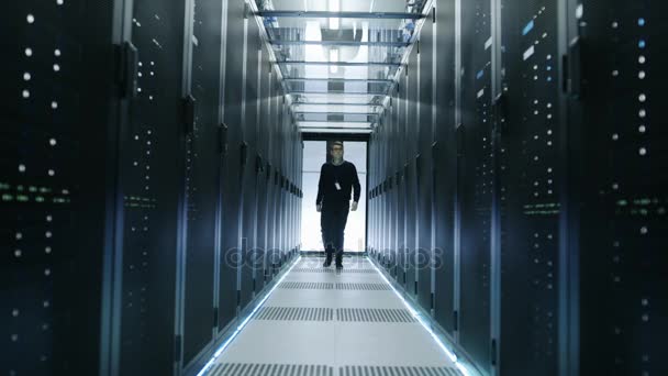 Vue frontale de l'ingénieur informatique marchant à travers le centre de données avec des serveurs de rack de travail
.  - Séquence, vidéo