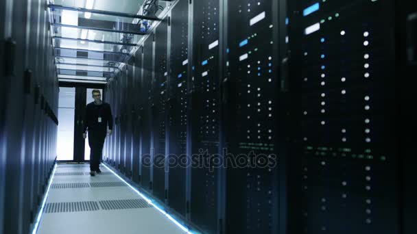 Vista frontal del Ingeniero de TI sosteniendo el cuaderno y caminando a través del centro de datos lleno de servidores de rack de trabajo
.  - Metraje, vídeo