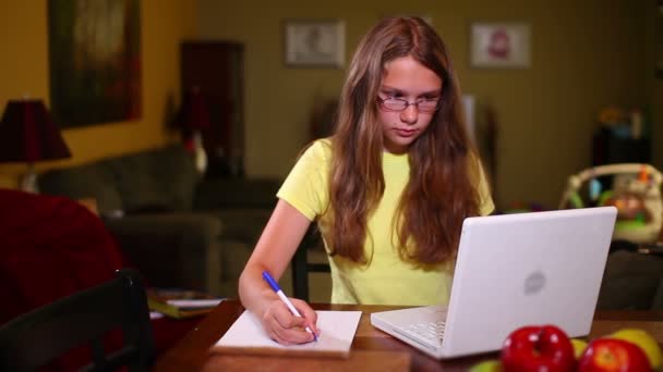 een jonge meisje doet haar huiswerk alleen op de keukentafel. - Video