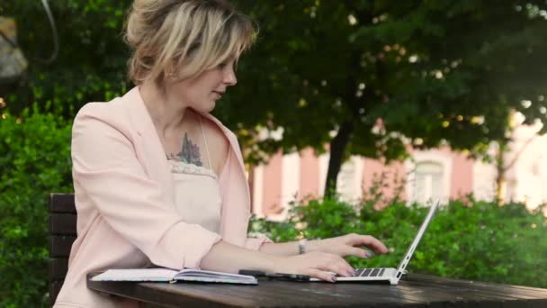 Atractiva rubia blanca que trabaja freelance con laptop y smartphone en el parque en un día soleado
 - Metraje, vídeo