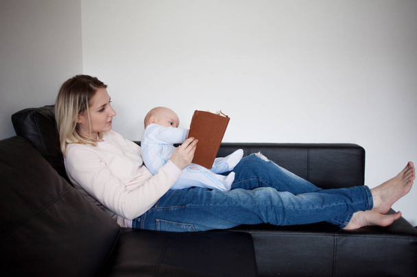 Young mother and her child reading a book, the concept of early development, indoor - Фото, изображение