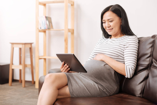 Positive asian pregnant woman using her tablet - Valokuva, kuva