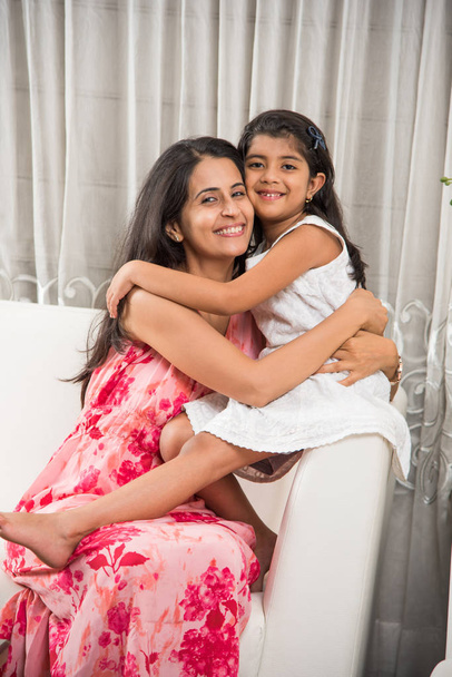 madre inteligente india abrazando a su linda hija, Retrato de la madre y la hija indias felices juntas mientras están sentadas en el sofá
 - Foto, Imagen