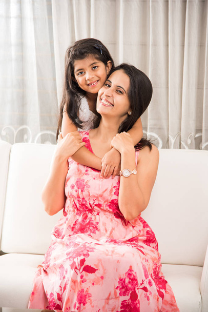 indian smart mother hugging her cute daughter, Portrait of happy Indian mother and daughter together while sitting on sofa - Foto, Imagen