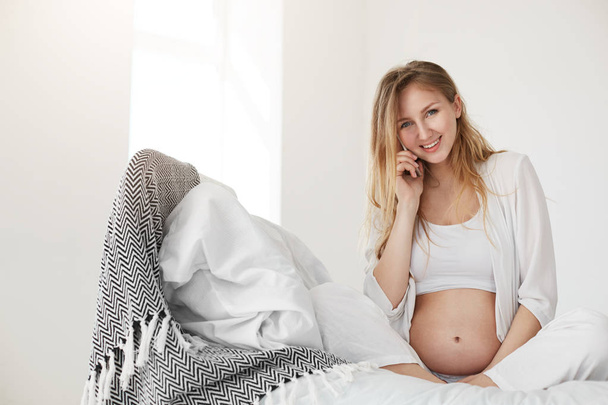 Prenatal consultation. Girl talking on phone to her gynecologist or baby doctor smiling relaxing enjoying her homestay - Fotó, kép