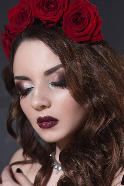 красивая молодая женщина с цветами роз в волосах. красотка с макияжем на темном фоне. темно-красные помады крупным планом
 - Фото, изображение