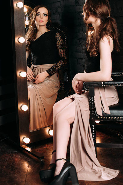 Individualität. Nachdenkliche elegante Dame im schwarzen Ballkleid, die neben Spiegel auf dunklem Hintergrund steht. Mode retuschiert Schuss - Foto, Bild