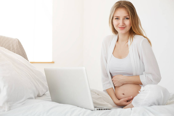 Pregnant woman using laptop at home. Online entrepreneur running her online store for kids apparel - 写真・画像