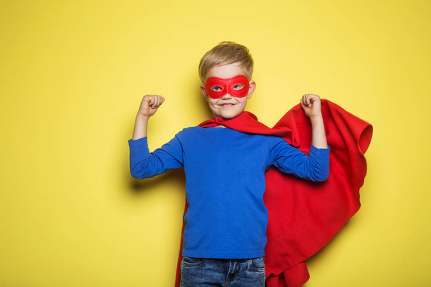 Junge in rotem Superhelden-Umhang und Maske. Übermensch. Studioporträt auf gelbem Hintergrund - Foto, Bild