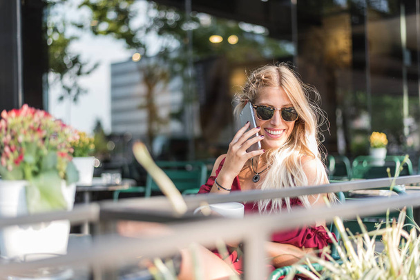 Joyeux blonde belle femme utilisant un téléphone mobile boire une tasse de café dans une terrasse à l'extérieur
 - Photo, image