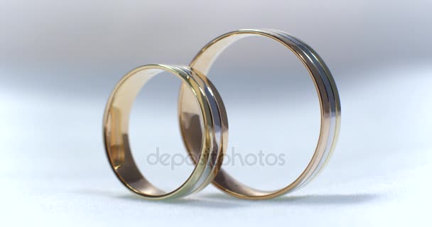 Two gold wedding rings lying on white-gray surface shining with light close up macro. Transfusion of light on rings. - Footage, Video
