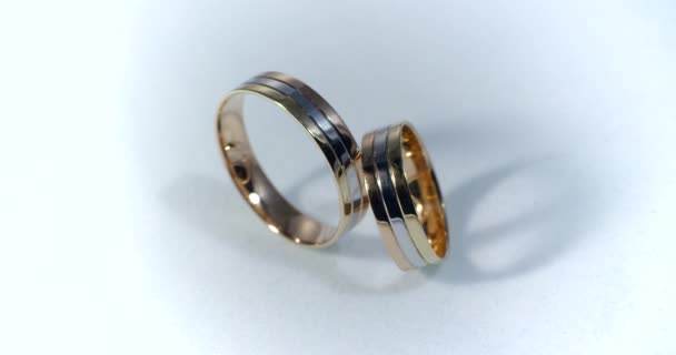 光輝くホワイト グレーを表面上に横たわる 2 つの金の結婚指輪は、マクロを閉じます。リング上の光の輸血. - 映像、動画