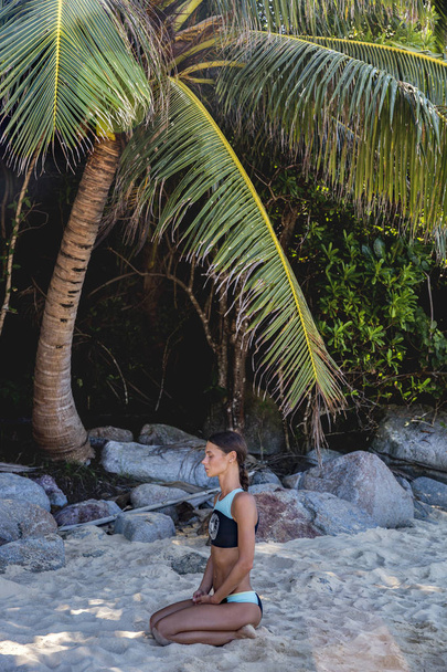 Młoda kobieta z dredami robi joga siedzi wśród drzew palmowych, - Zdjęcie, obraz