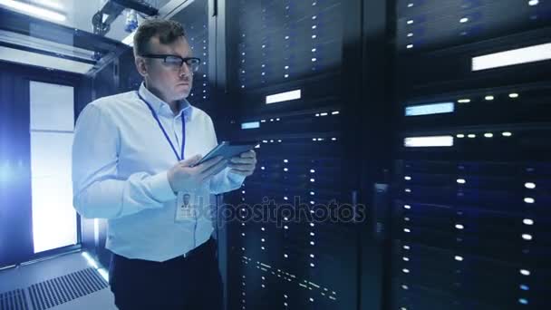Following Shot of IT Engineer Walking Through Data Center Corridor with Rows of Rack Servers. He Uses Tablet Computer. - Footage, Video