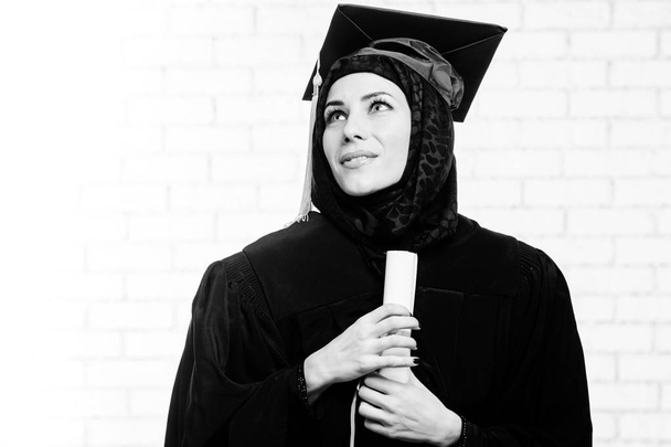 Щасливий аспірант мусульманської студентки з дипломом у приміщенні. Чорно-біла картина
. - Фото, зображення
