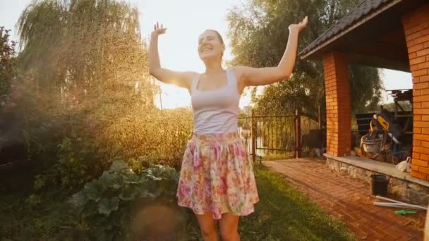 Zeitlupenvideo einer tanzenden Frau im Sonnenuntergang unter Wasser aus der Gartensprengung - Filmmaterial, Video