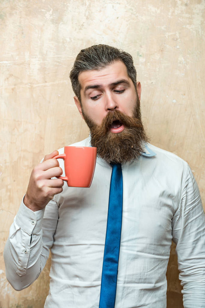 bearded man with curious face look into tea, coffee cup - Photo, image