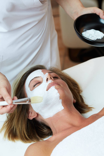 Beautiful young woman having a facial cosmetic mask at spa salon - Photo, Image