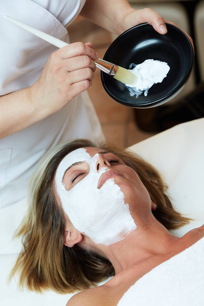 Beautiful young woman having a facial cosmetic mask at spa salon - Photo, Image