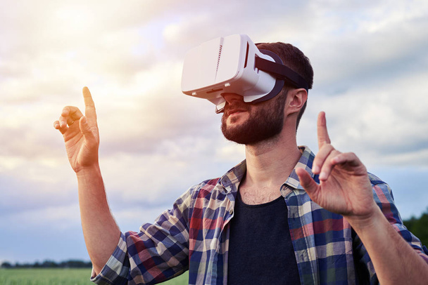 Человек в очках виртуальной реальности масштабирует объект, стоя в зеленом поле
 - Фото, изображение