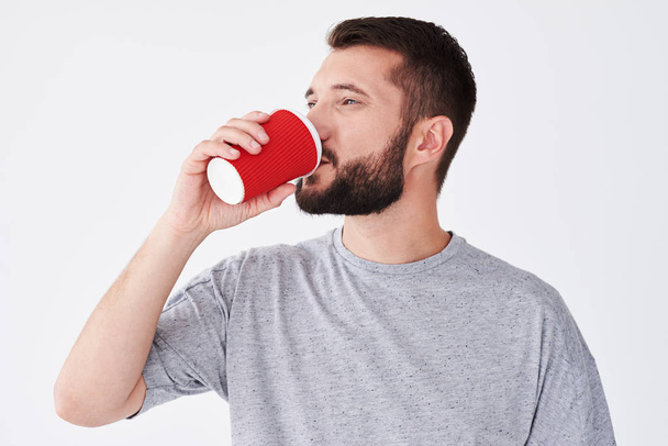 Smiling bearded man tasting coffee from paper glass  - Fotografie, Obrázek