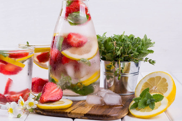 Agua mineral infundida con fresas, hielo, hierbas y hojas de menta sobre fondo blanco, agua de desintoxicación casera
 - Foto, imagen