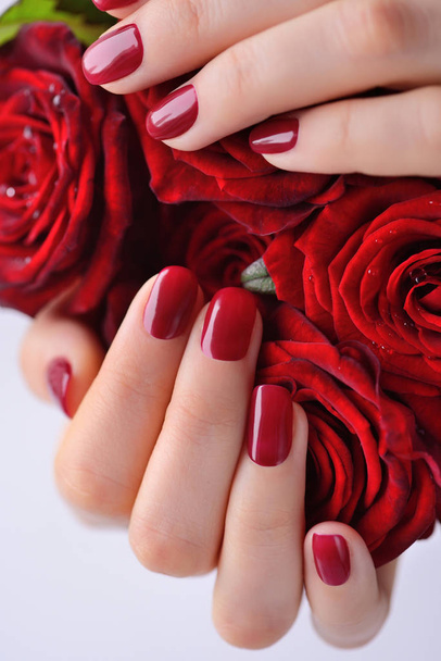 Hände einer Frau mit roter Maniküre mit einem Strauß roter Rosen. Nahaufnahme - Foto, Bild