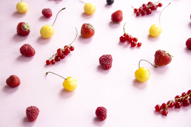 Summer berries are scattered on a pink background - currants, cherries, raspberries and strawberries - Photo, image