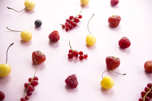 Summer berries are scattered on a pink background - currants, cherries, raspberries and strawberries - Zdjęcie, obraz