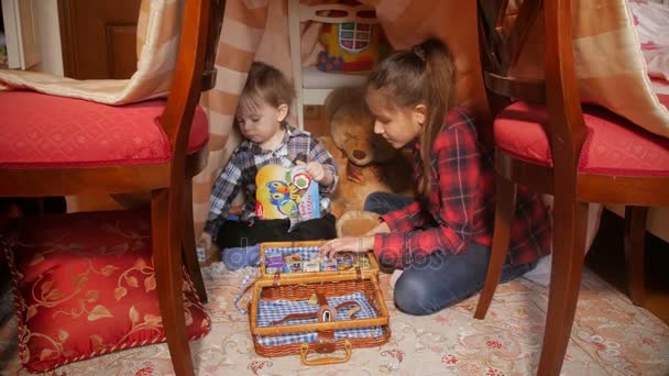 Niño jugando con hermana en tienda de campaña hecha de mantas en la sala de estar
 - Metraje, vídeo