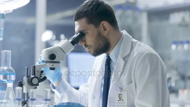 Výzkumný vědec vypadá do mikroskopu a píše se jeho pozorování. Pracuje v moderní laboratoře. - Záběry, video