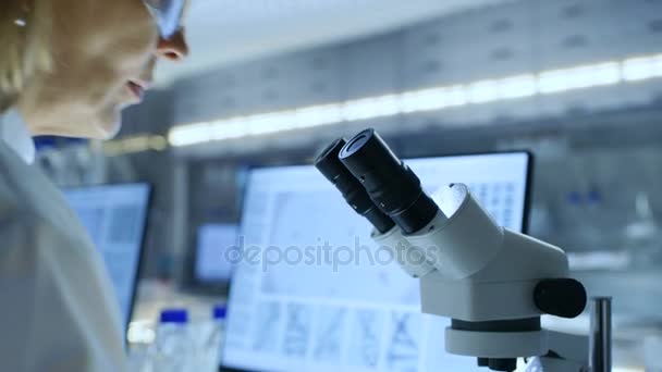 Senior női biológus működik a számítógép és úgy néz ki, az anyagok Mikroszkóp alatt. Shes '-ban egy Modern laboratóriumi. - Felvétel, videó