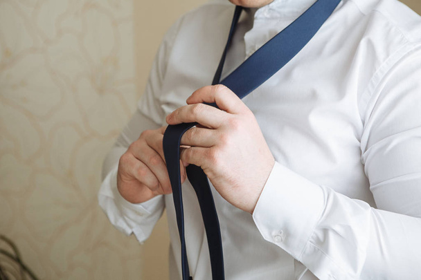 People, business, fashion and clothing concept - close up of man in shirt dressing up and adjusting tie on neck at home. Businessman putting on a tie. Man putting on necktie. Dressed in the morning - Foto, Bild