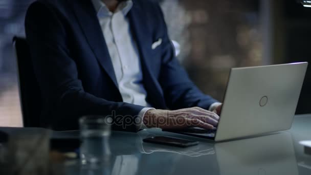 Поздно ночью бизнесмен работает над ноутбуком в своем личном кабинете с видом на окно большого города
. - Кадры, видео