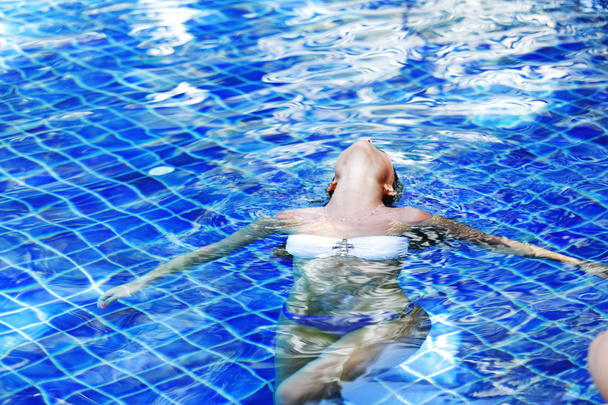 Woman floating in swimming pool - 写真・画像
