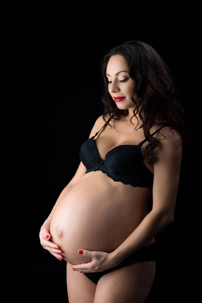 Portrait of a beautiful pregnant woman in black lingerie, studio on a black background - Fotó, kép