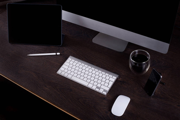 czarny ekran komputera w pokoju na brązowym biurku i kamery filmowania, kubek kawy, telefon, Tablet PC, na ciemnym ścianie - Zdjęcie, obraz