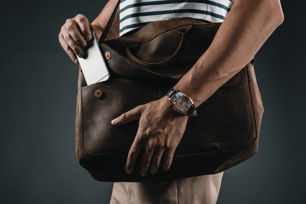 man putting smartphone into bag - Zdjęcie, obraz
