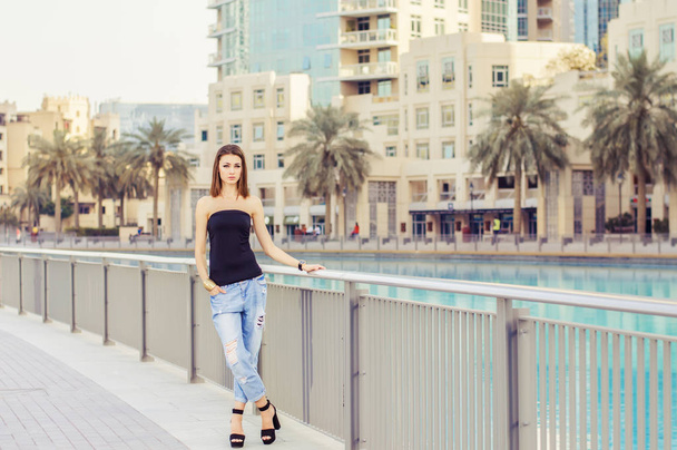 Mujer joven con bob corte de pie cerca de la valla de metal en el centro de Dubai. Fashionista con el pelo castaño de pie en la calle vacía en traje casual
 - Foto, imagen